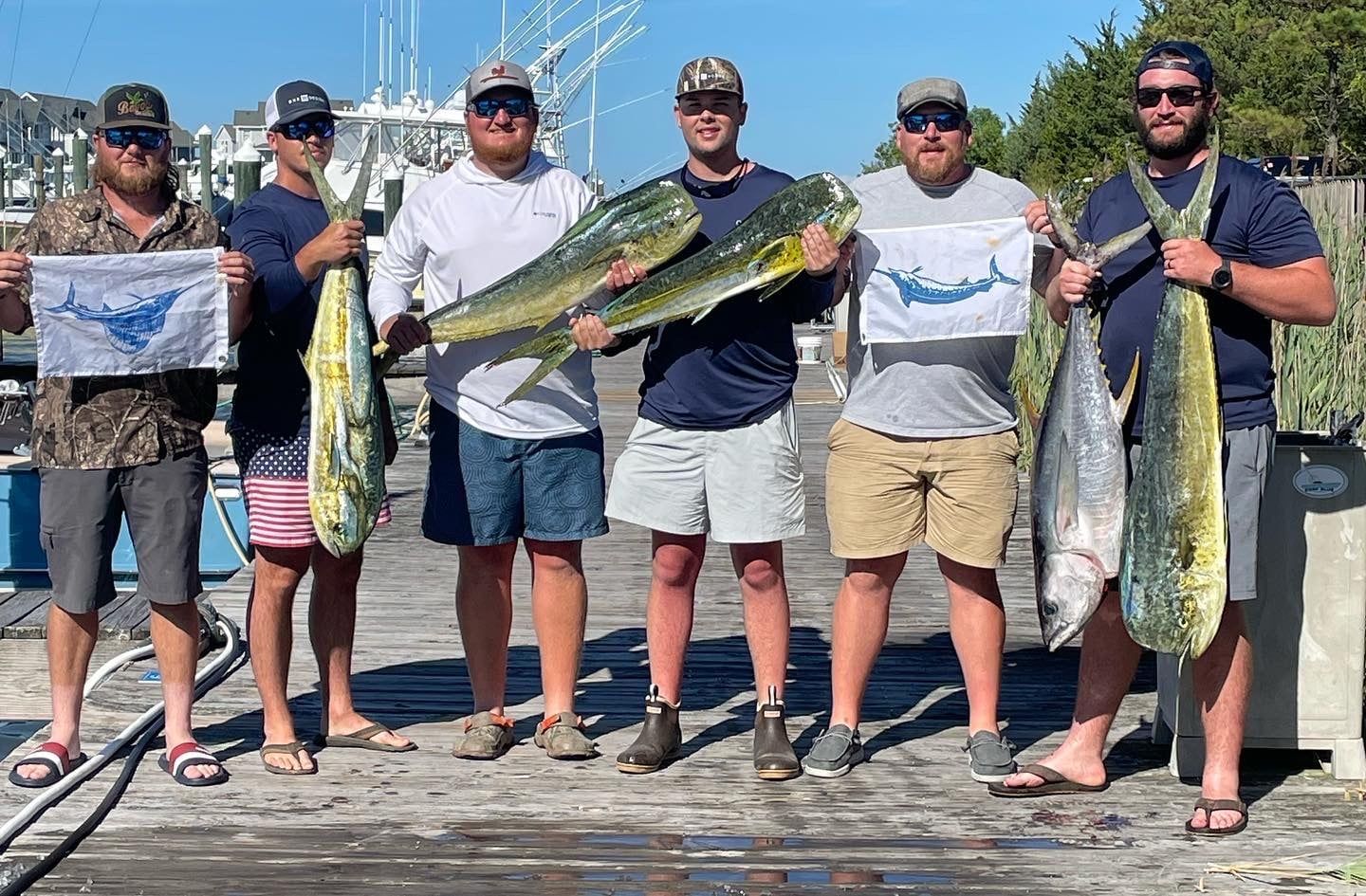 A group of men are standing on a dock holding fish.