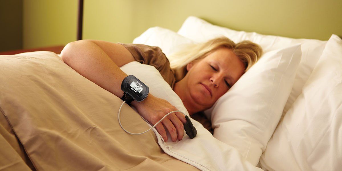 Blond woman sleeps with a pulse reader attached from her index finger to her wrist.