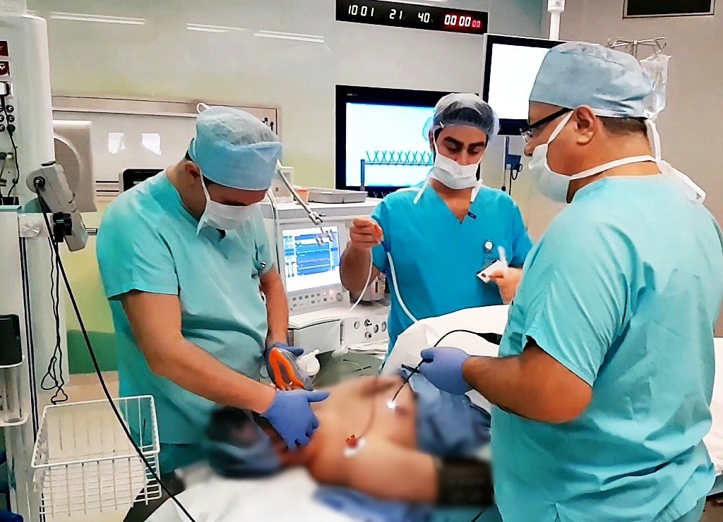 Three surgeons in scrubs and masks performing surgery for Obstructive Sleep Apnea on a patient laying on an operating table.