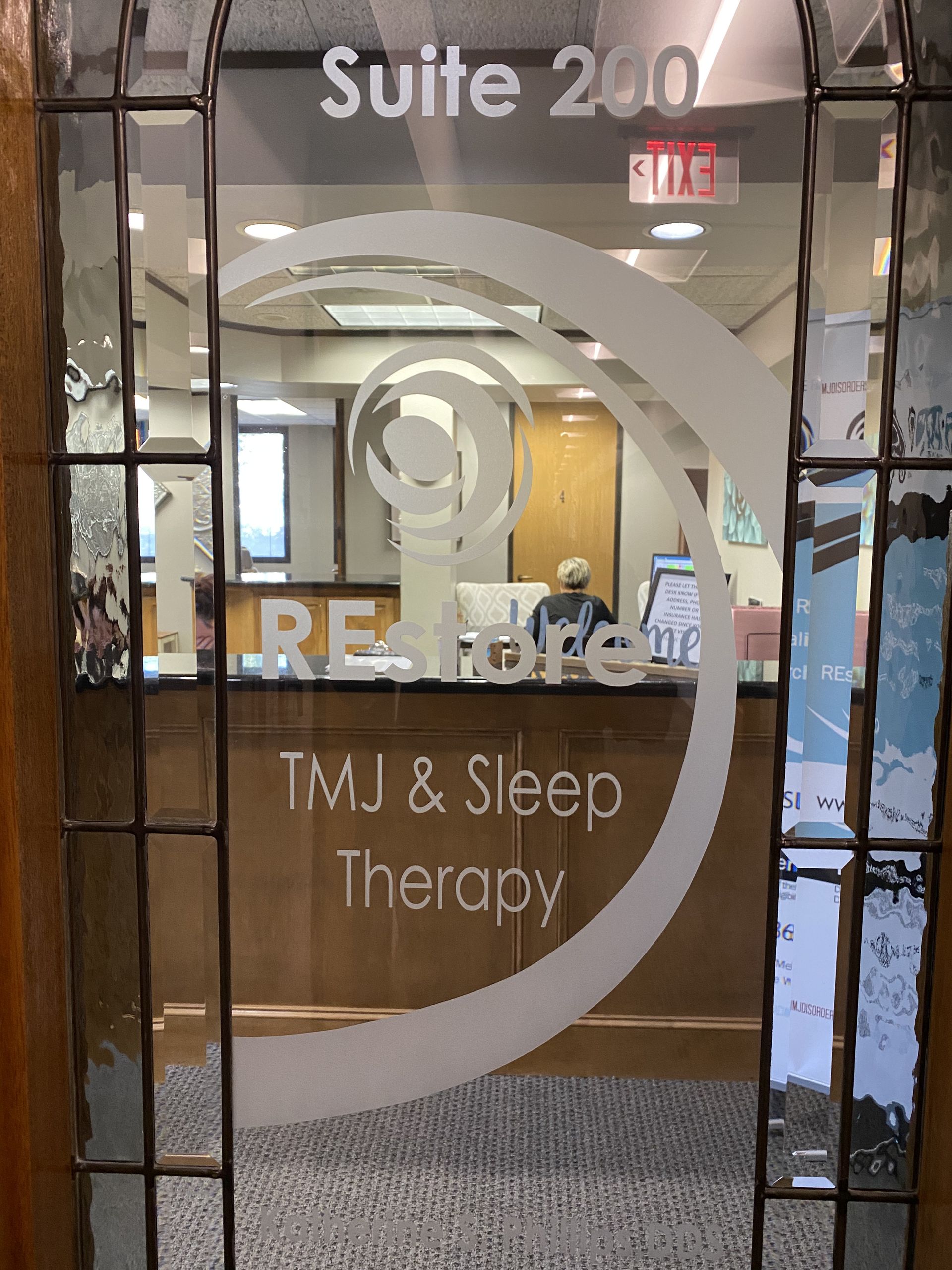 Close look through the glass into the front entrance of the Restore TMJ offices showing someone working at the front desk.