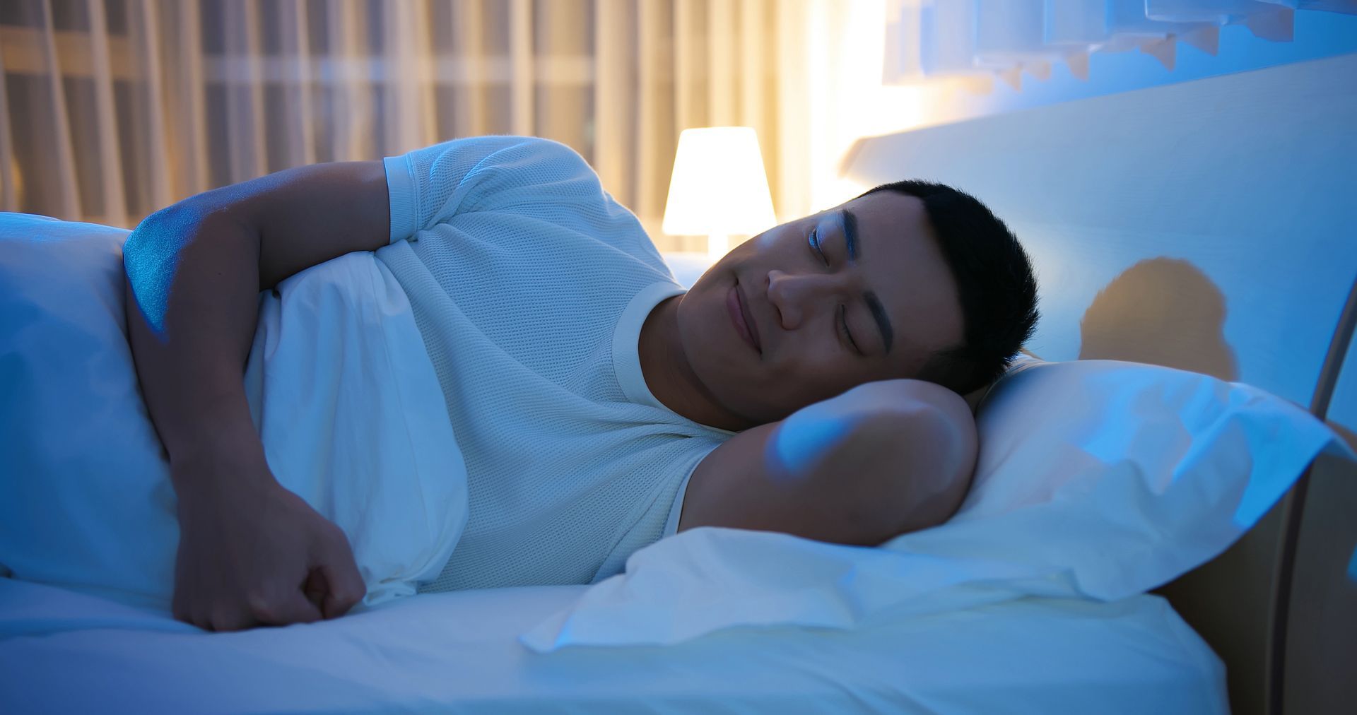 Man smiling while sleeping in a bed with white sheets. 
