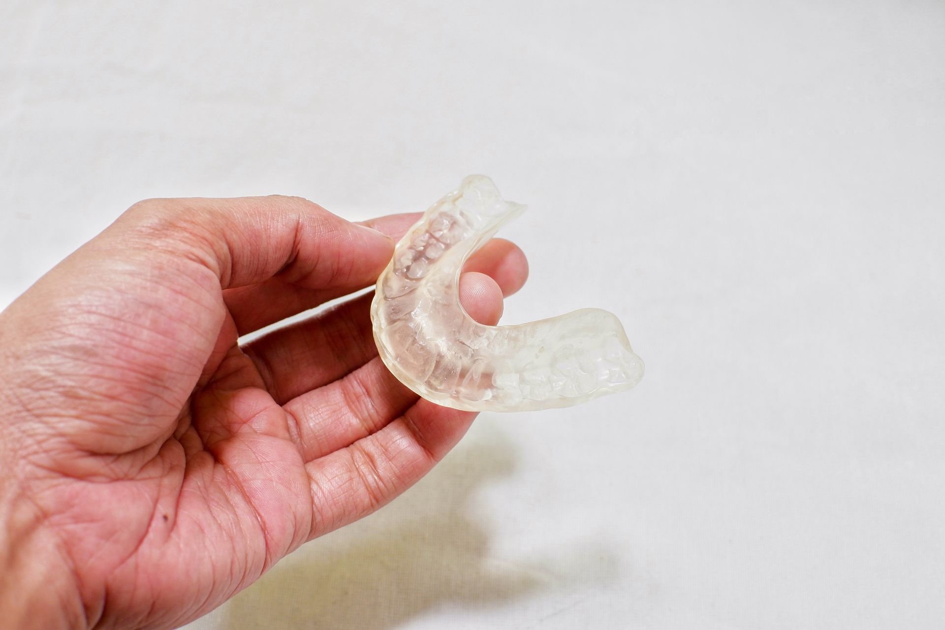 Close-up of a hand holding an oral splint appliance used for treatment of TMD and TMJ pain.