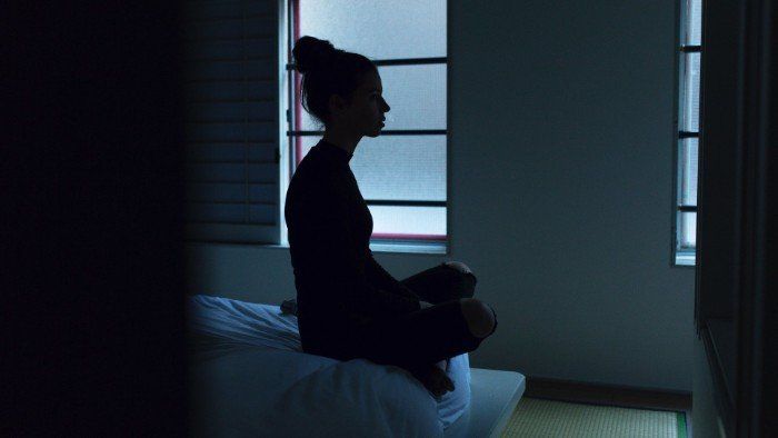 Dark profile view of young woman sitting awake at night while experiencing insomnia.