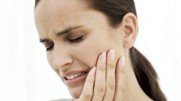 Women with brown hair holds her jaw while grimacing in pain from TMJ symptoms.
