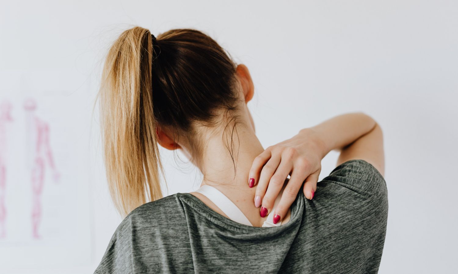 Back view of woman in grey shirt experiencing muscle pain while touching her neck