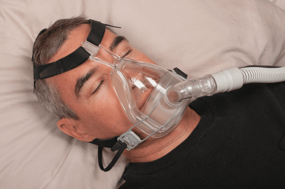 Middle aged man laying in bed with a CPAP mask on while sleeping. 