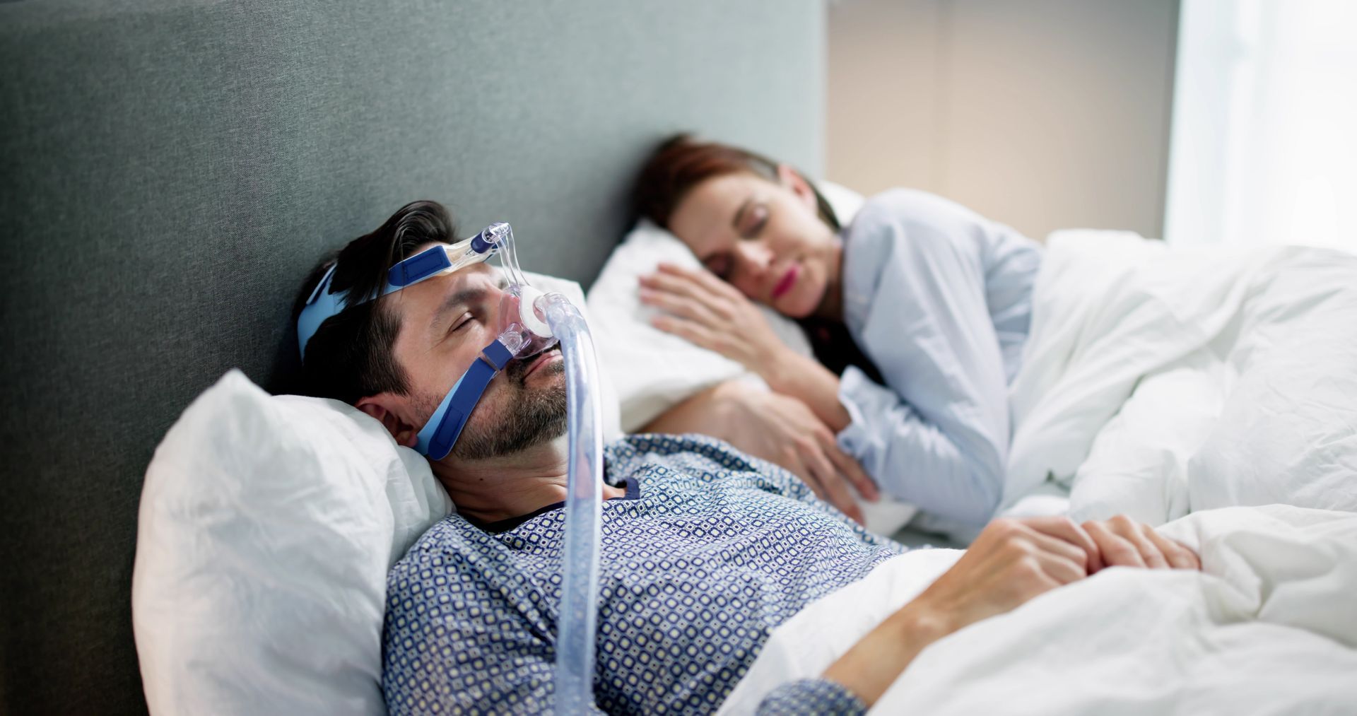 Middle aged man in pajamas sleeps next to his spouse while wearing a cpap mask.