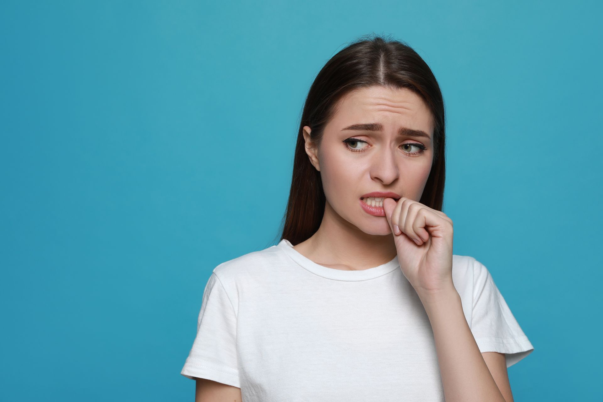 Young woman experiencing stress and anxiety bites her thumbnail.