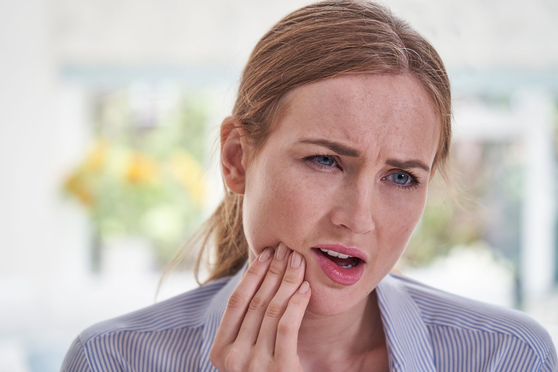 Young woman with red hair presses fingers to her jaw while sensing tmj pain.