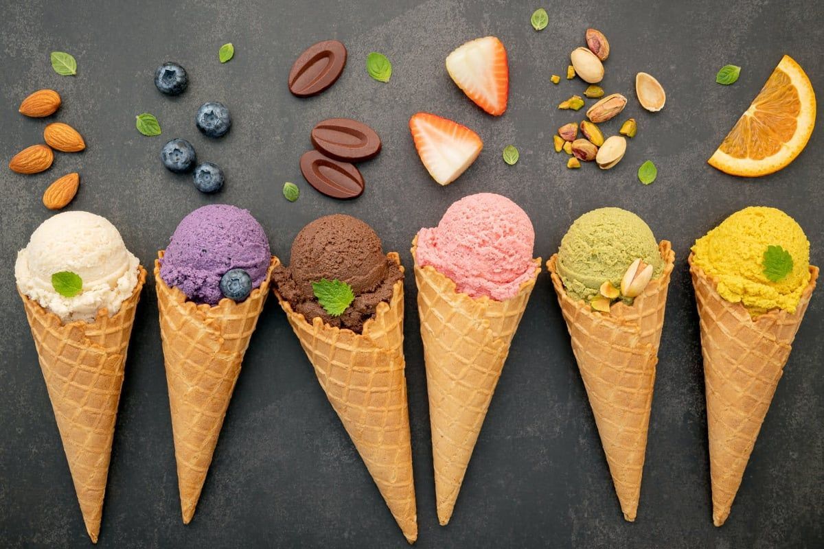 Six ice cream cones with various flavors and toppings arranged on a dark surface.