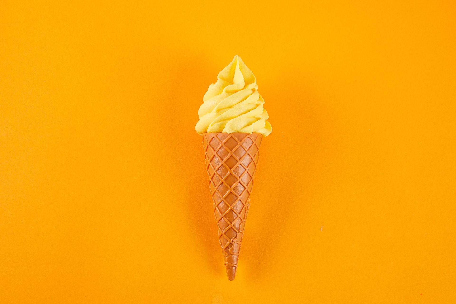 Yellow soft-serve ice cream cone against a solid orange background.