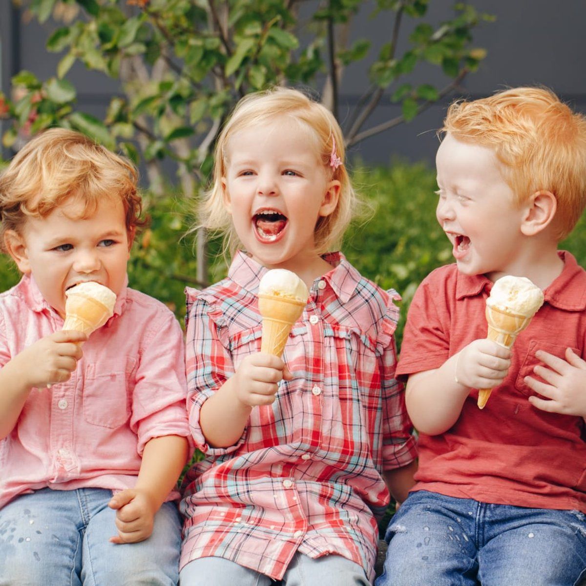 Three young children enjoying ice cream cones outside.