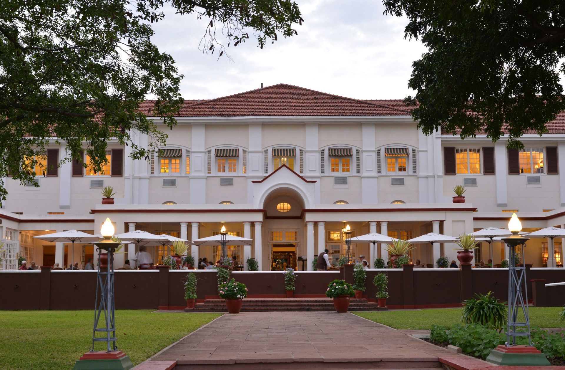 A two-story, cream-colored historic building with a red-tiled roof and arched entryway, viewed across a manicured lawn.
