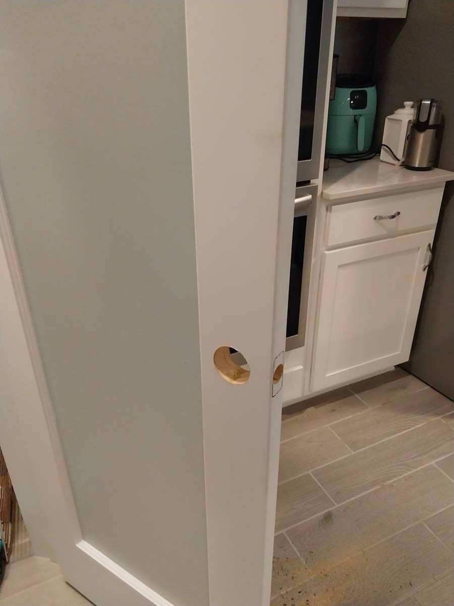 A white door with a hole in it is open to a kitchen.