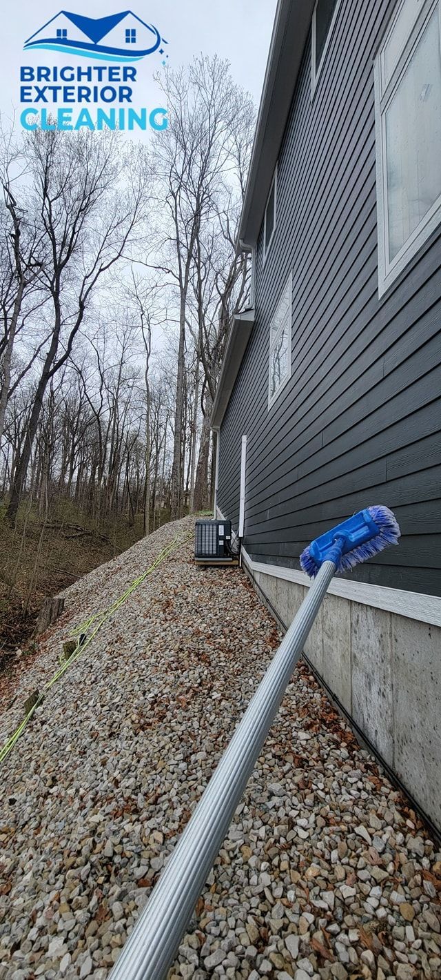 A person is cleaning the side of a house with a broom.
