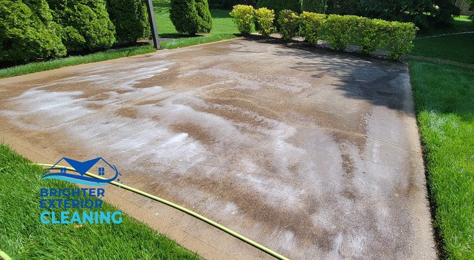 A concrete driveway is being cleaned with a hose.