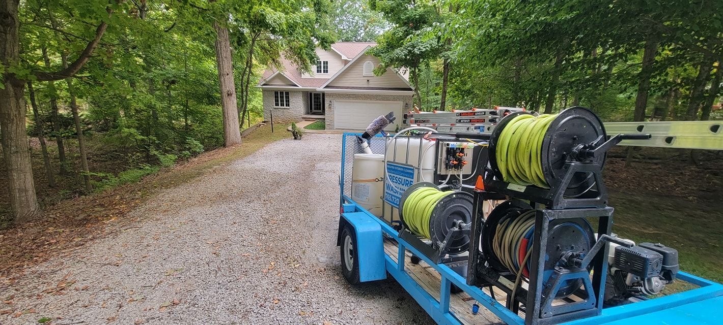 A trailer with a hose reel attached to it is parked in front of a house.