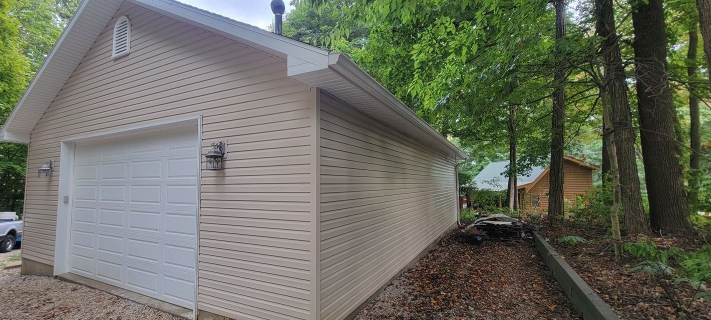A white garage with a white door is sitting in the middle of a forest.