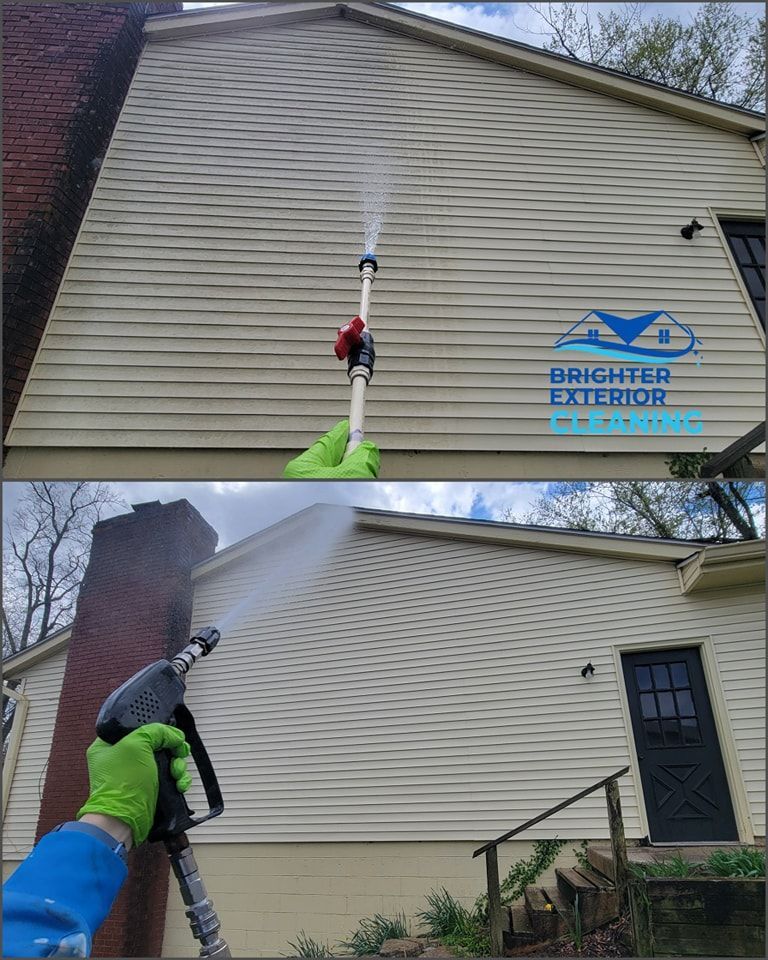 A person is cleaning the side of a house with a pressure washer.