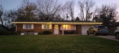 A house with christmas lights on the roof and a car parked in front of it.