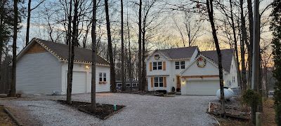 A house with a garage and a driveway in the middle of a forest.