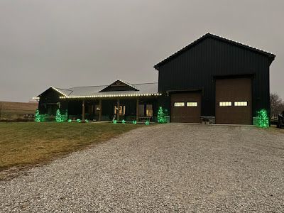 A large black barn is decorated with christmas lights and green trees.