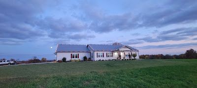 A large white house is sitting in the middle of a grassy field.