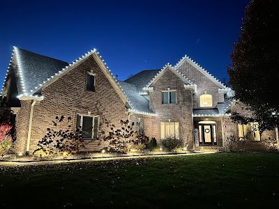 A large brick house is lit up with christmas lights at night.