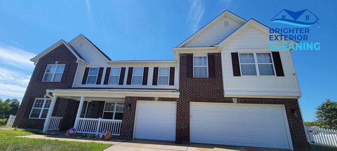 A large brick house with white garage doors and shutters on a sunny day.