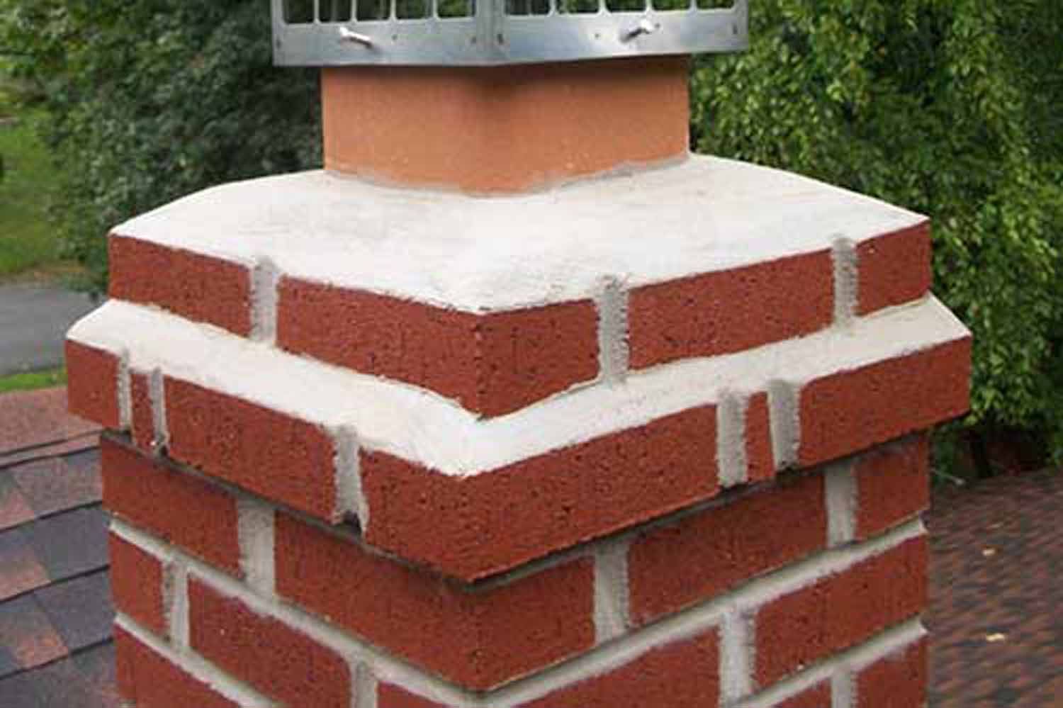 Brick chimney with white mortar, a metal cap, and angled top.