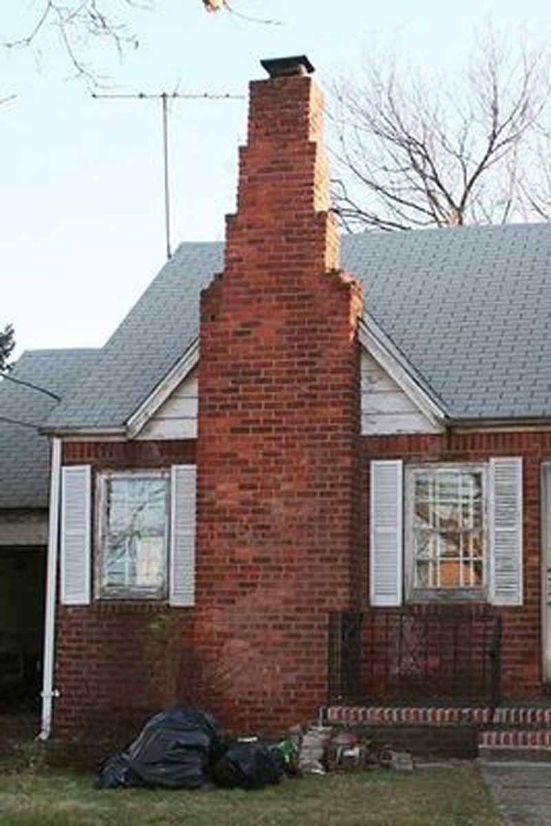 Red brick chimney on a house with white shutters. Bags of trash are on the ground in front.