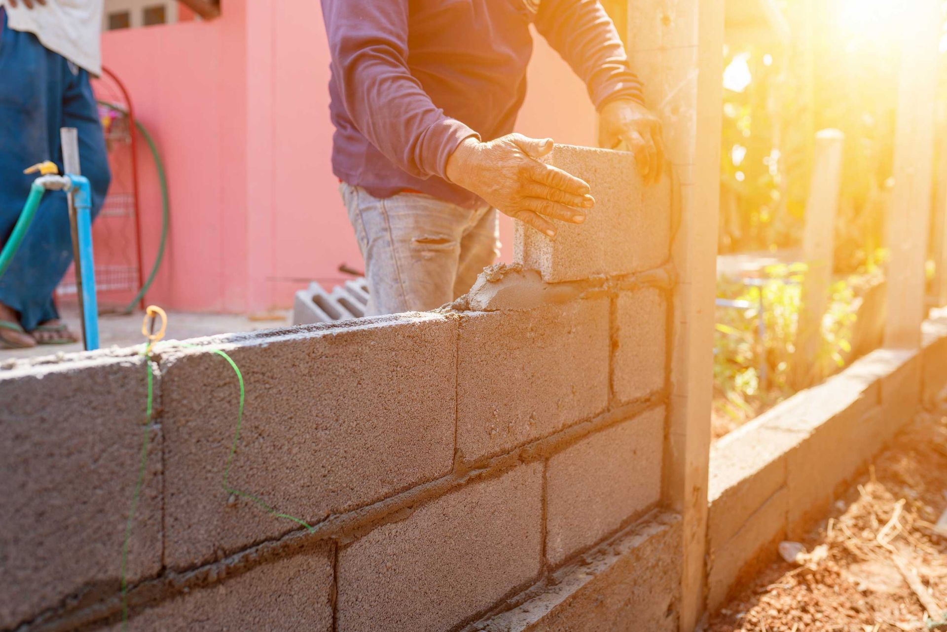 A worker is laying concrete blocks to build a wall at a construction site in bright sunlight A worker is laying concrete blocks to build a wall at a construction site in bright sunlight