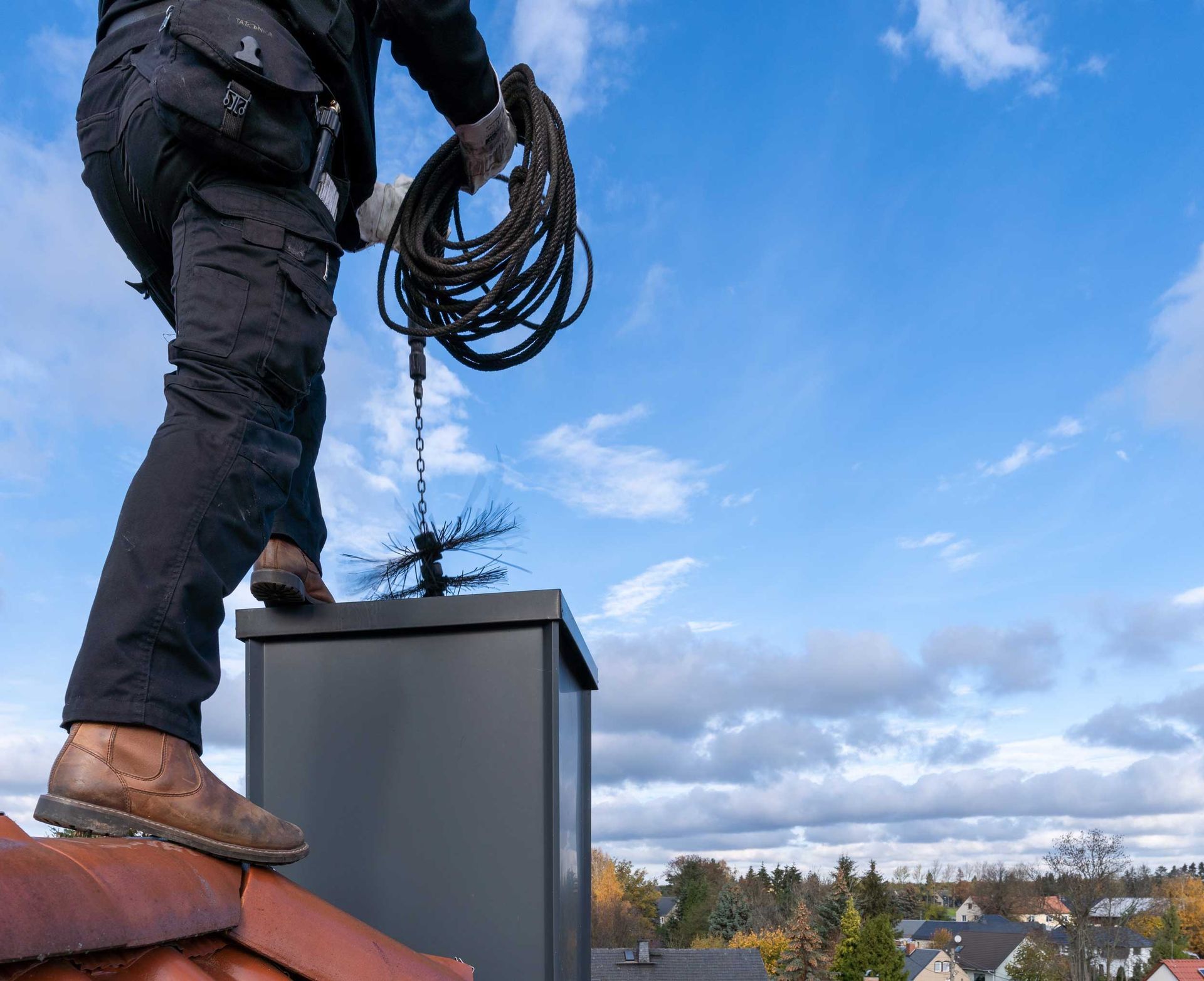 Chimney sweep man in work uniform cleaning chimney on building roof.