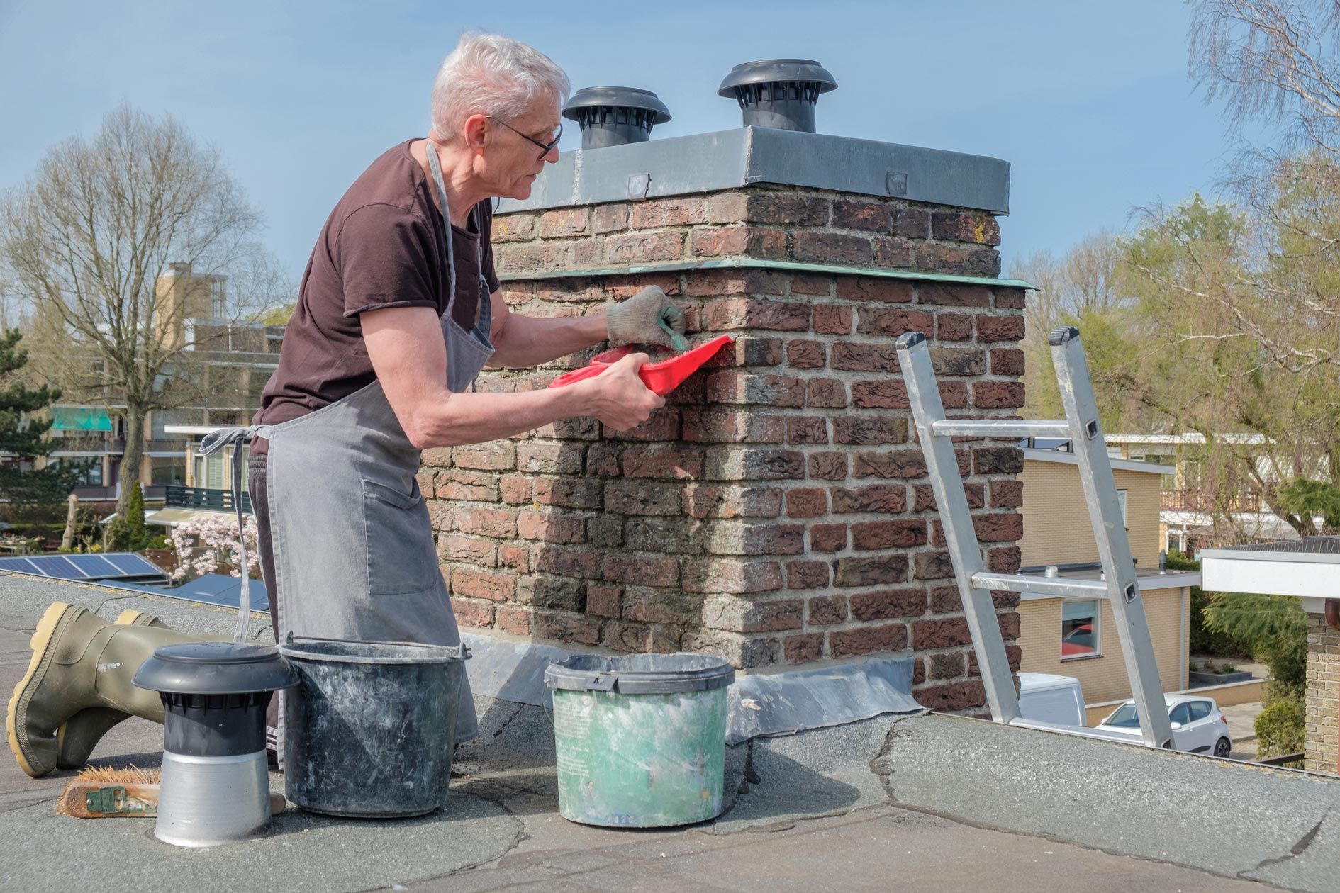A man repairing a brick chimney on a rooftop using a trowel and mortar A man repairing a brick chimney on a rooftop using a trowel and mortar
