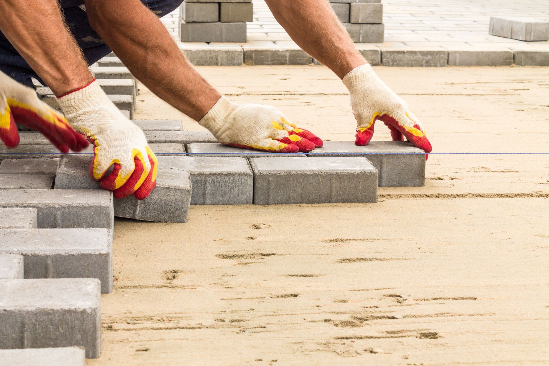 Close-up of masonry installation contractors, wearing gloves, laying paving tiles on the pavement.