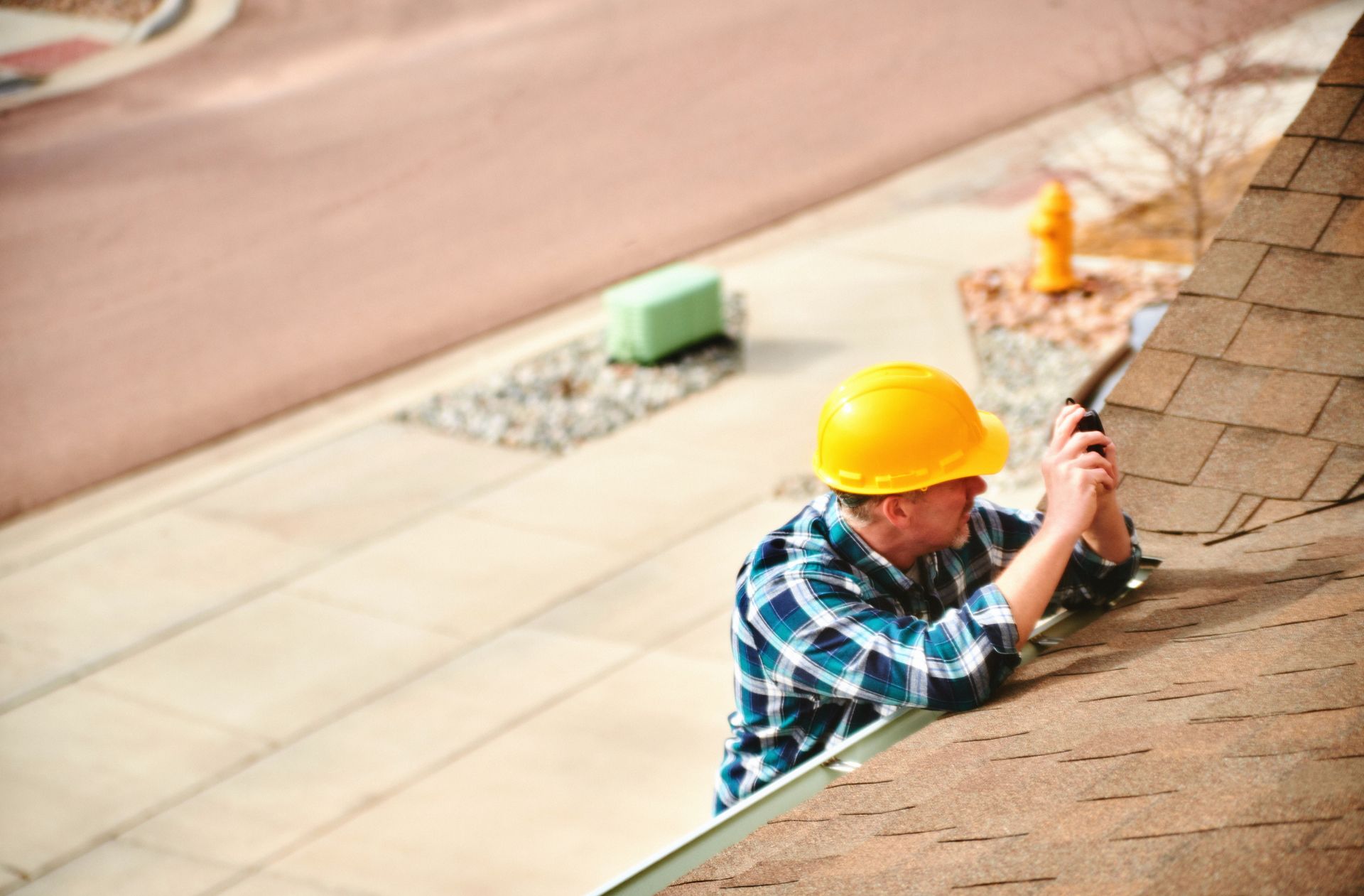 Worker in yellow hard hat installing shingles on a sloped roof.