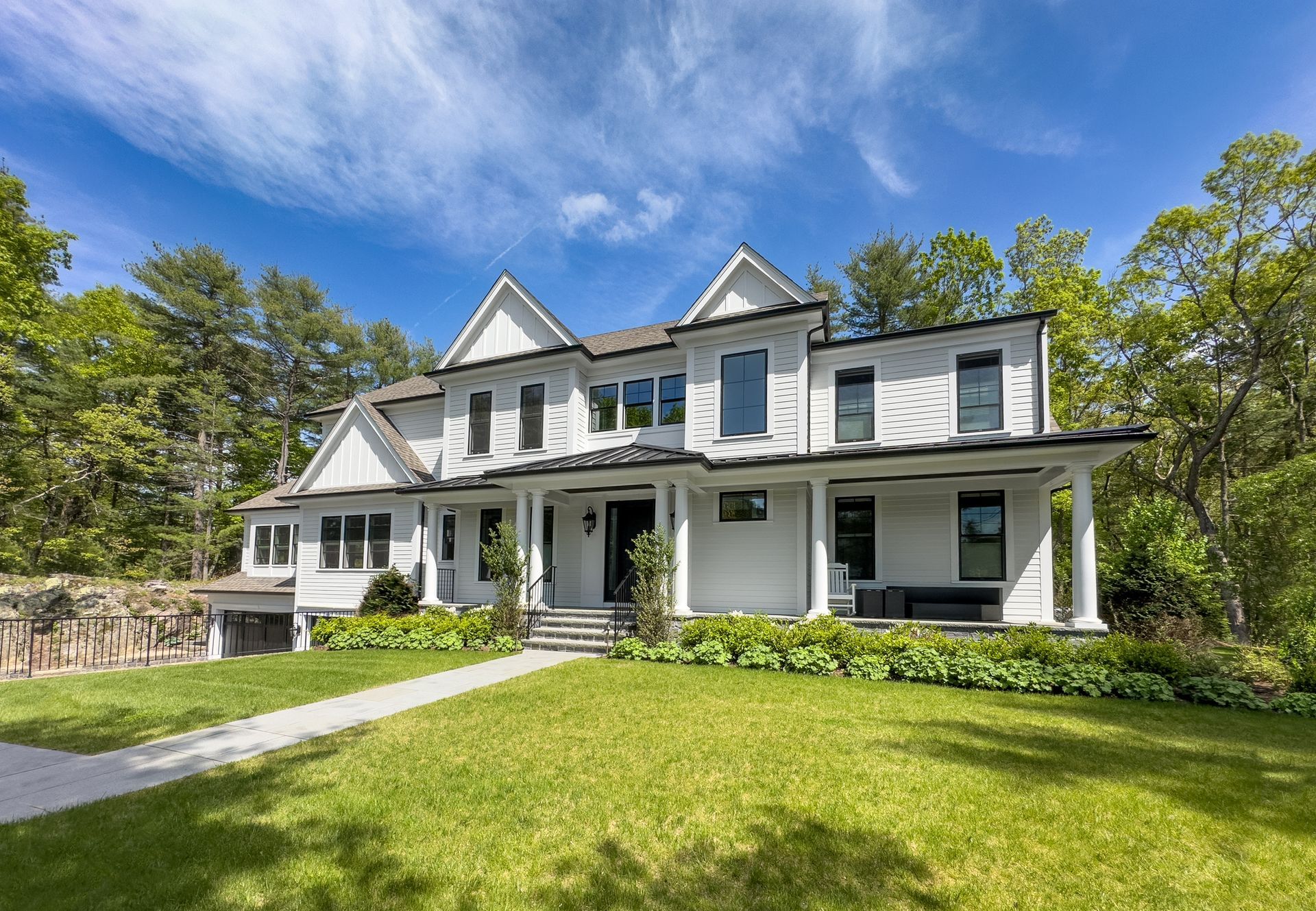 White two-story house with black trim, a covered porch, and a green lawn under a blue sky.
