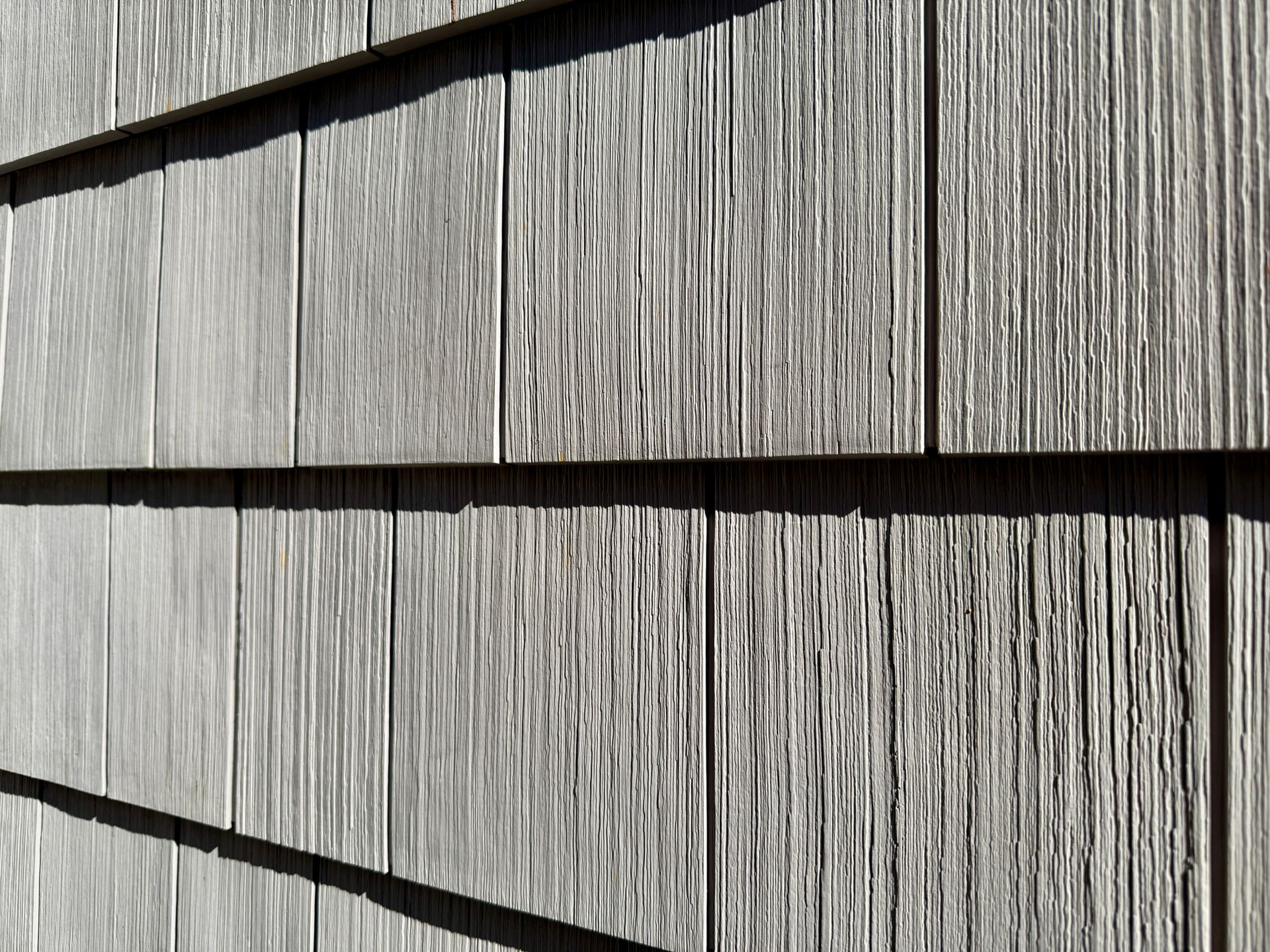 Gray weathered wood shingles with strong vertical grain, casting long horizontal shadows.