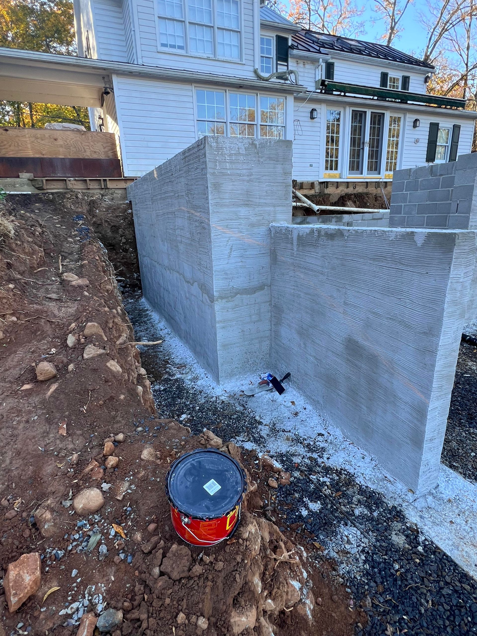 Foundation walls under construction next to a house with white siding and large windows.