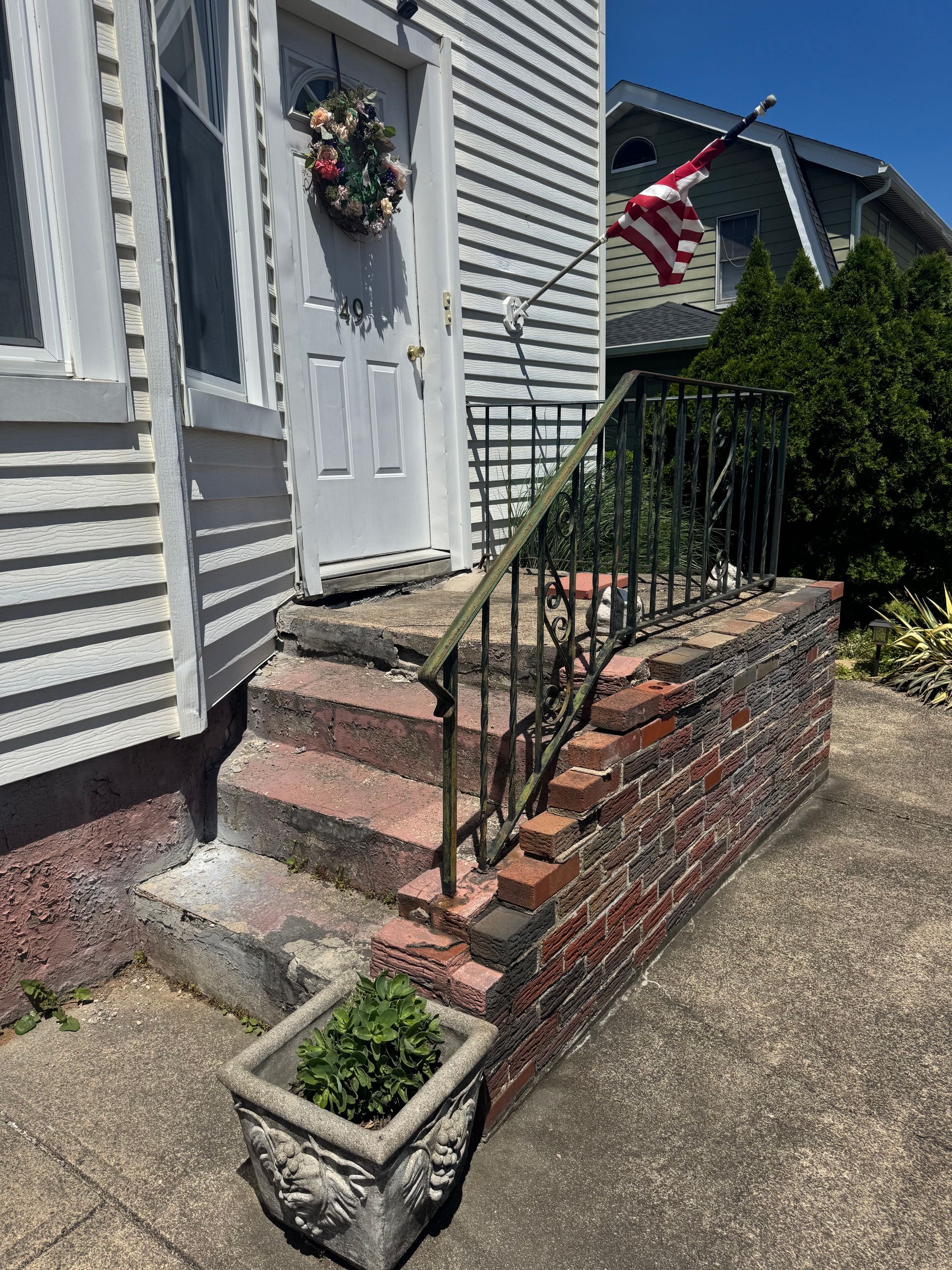 Exterior of a building with three brick and concrete steps leading to a white door with a wreath.