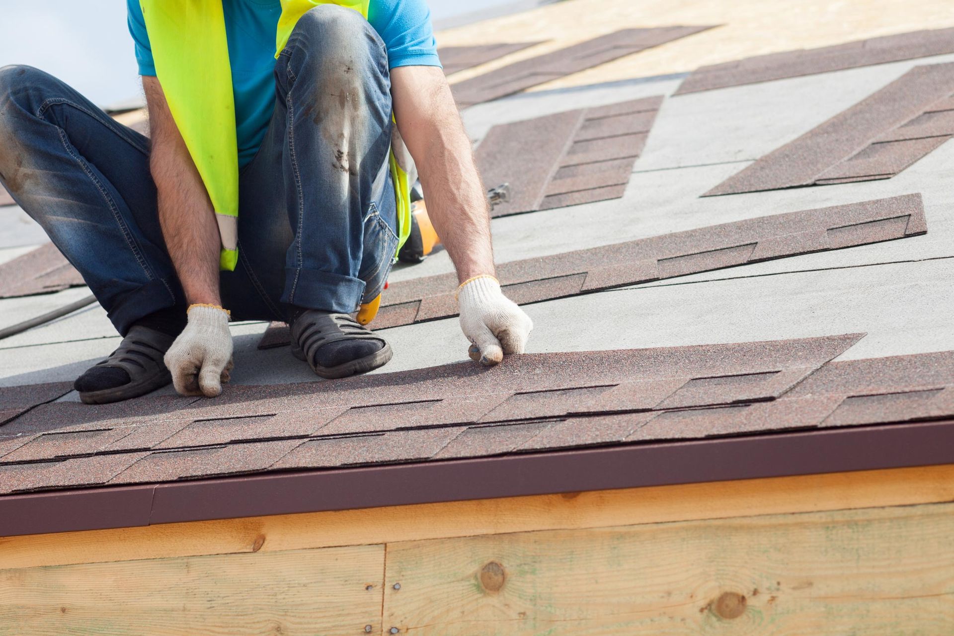 Worker installing asphalt shingles on a roof during residential roofing construction.
