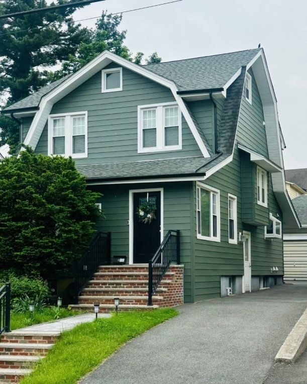 Two-story green house with black door, white trim, steps, and asphalt driveway.