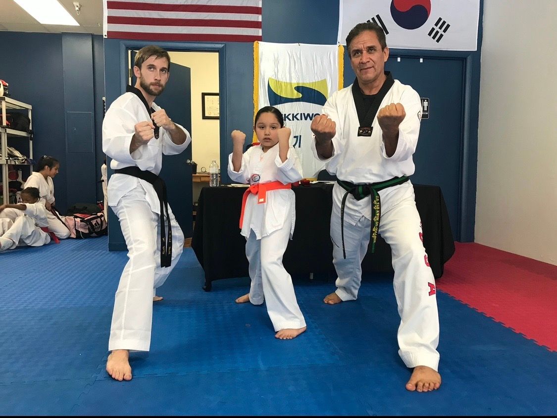 A martial arts instructor demonstrates a defensive technique with a student on a mat in a training studio.