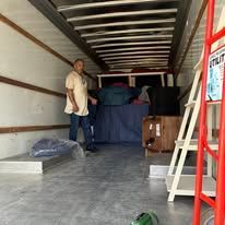 Man standing inside a truck. Cargo and furniture are visible.