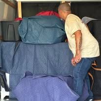 Man in a yellow shirt leaning over a stack of blue and purple blankets.