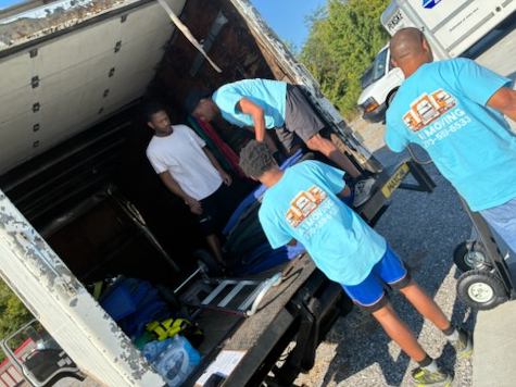 Two movers loading cardboard boxes into the back of a moving truck on a residential street.