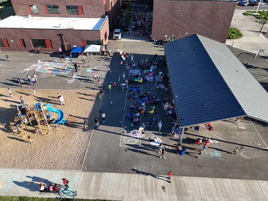 Aerial view of a schoolyard with children gathered; playing, under a shaded area and at a playground.