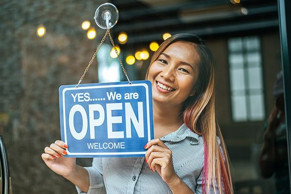 A woman is holding an open sign in front of a store door.
