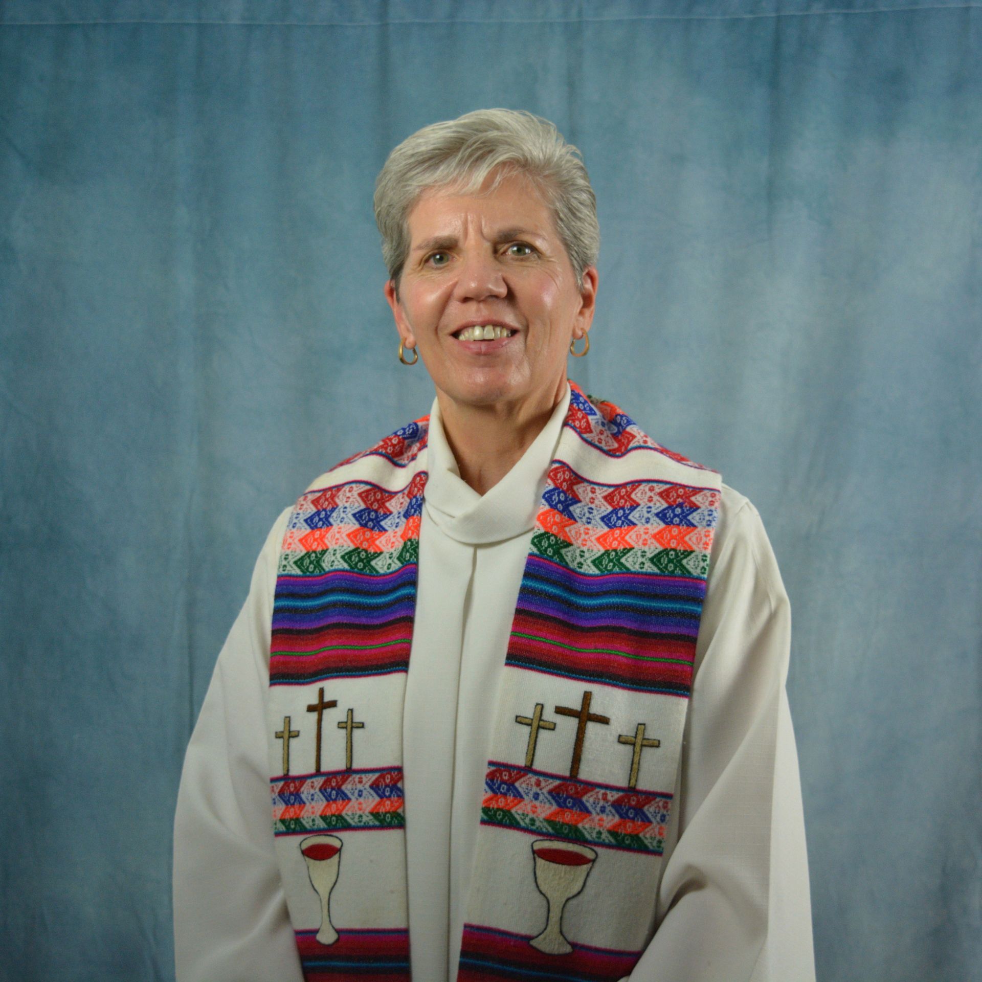 A woman in a black and white jacket is smiling in front of a stained glass window