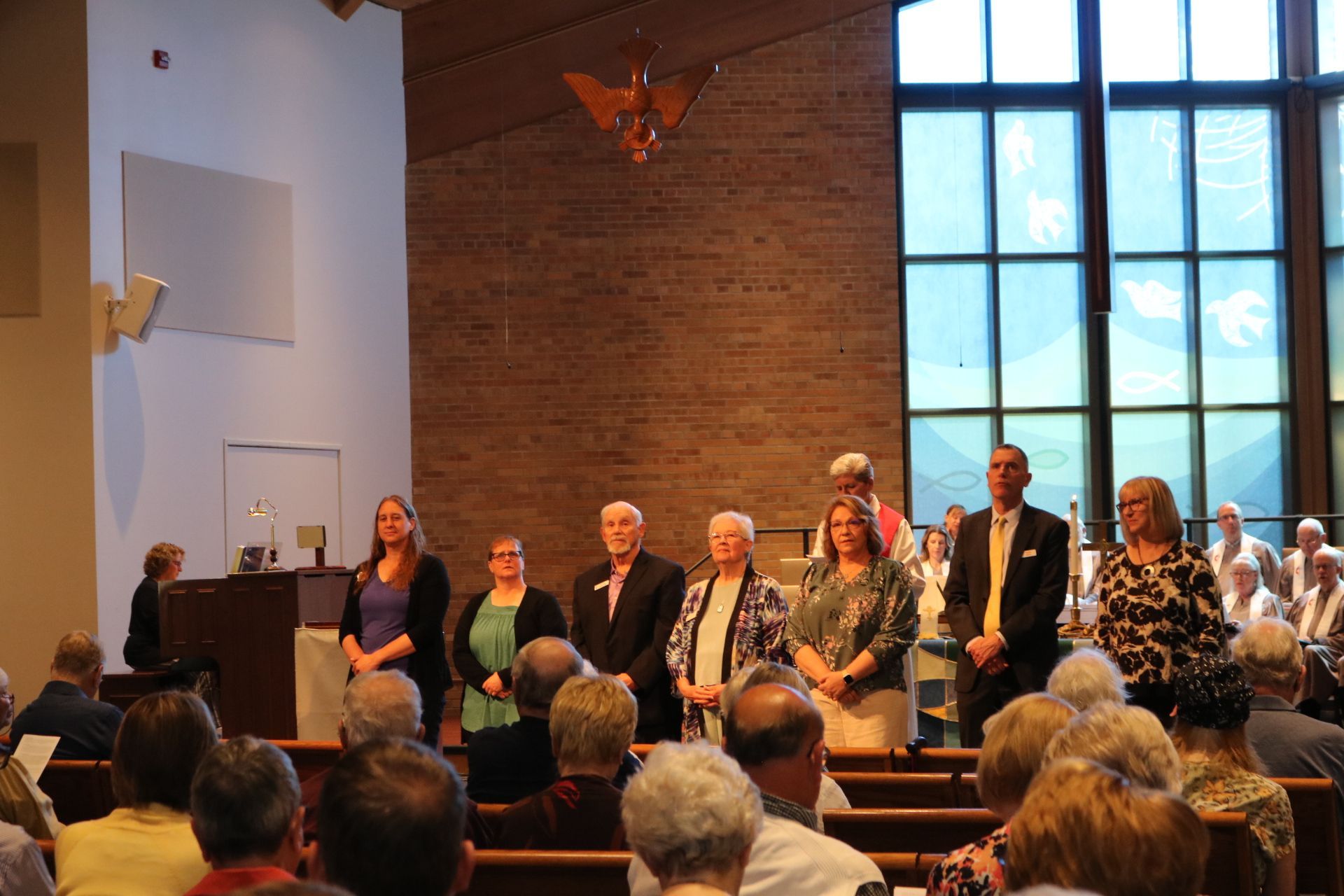 A group of people are standing in a church in front of a large window.